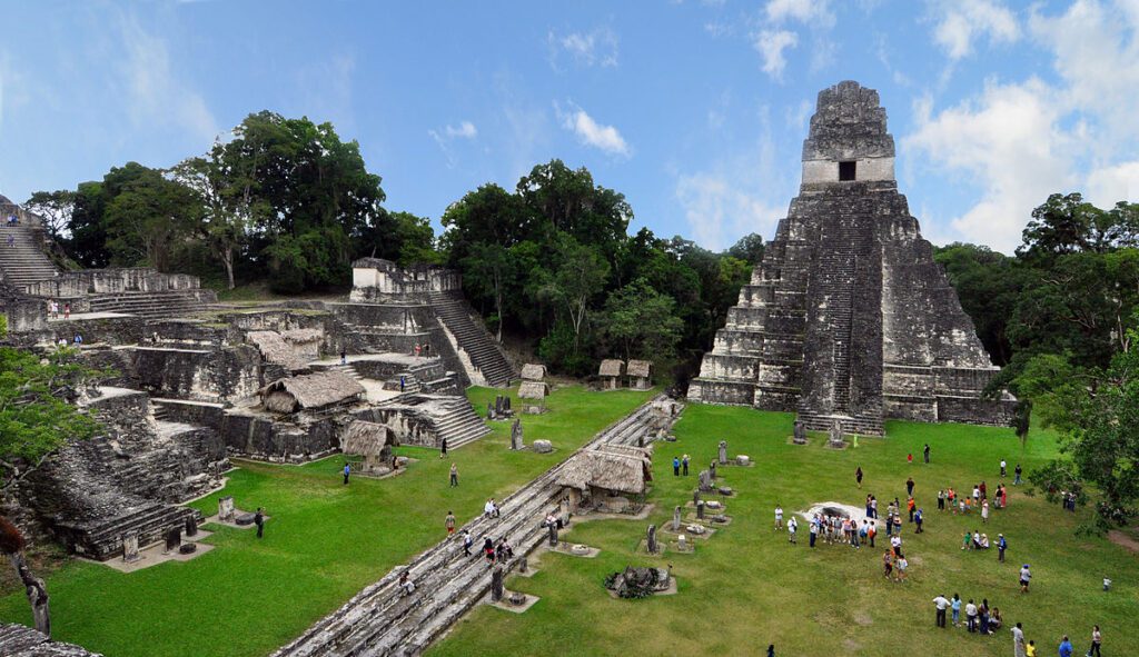 Monumental core at Tikal: temples rise above the canopy; LiDAR extends the scene into thousands of mapped platforms and paths outside the photo frame.