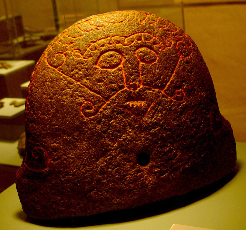 Face carved on a hearthstone with stitched lips, widely identified as the Norse trickster Loki.